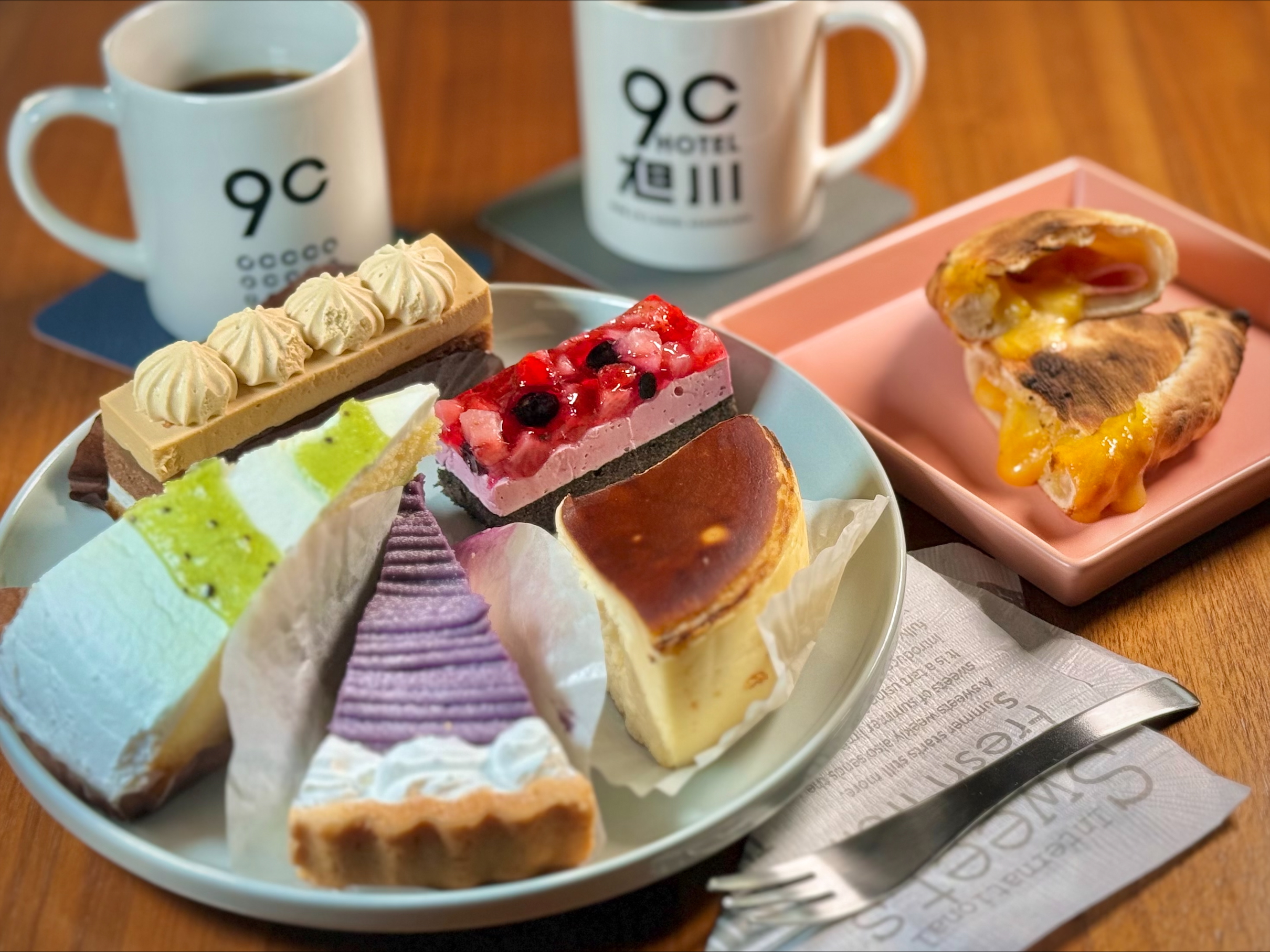 5種類のケーキが盛られた白いプレートとコーヒーが並ぶテーブル。9Cホテル旭川カフェバーで期間限定提供されるケーキプレート。